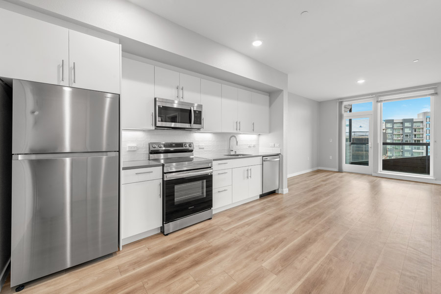 01_openfloor Open-concept living area and kitchen with stainless steel appliances, wood-look flooring, and large windows