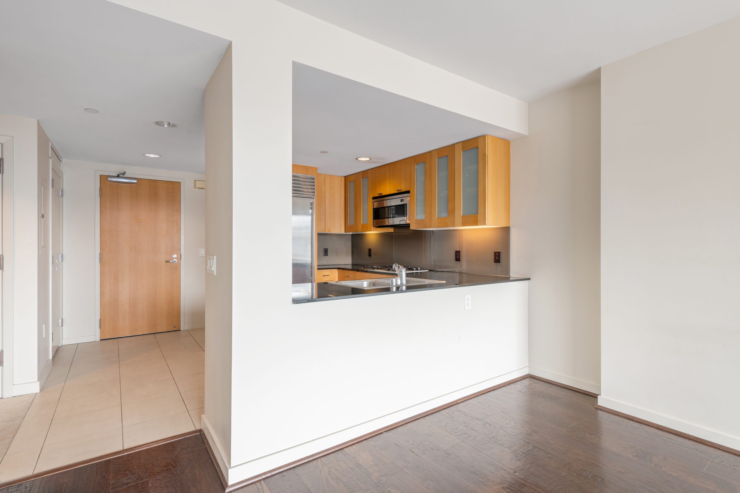 Open kitchen with breakfast bar, wood cabinetry, and view into living area.
