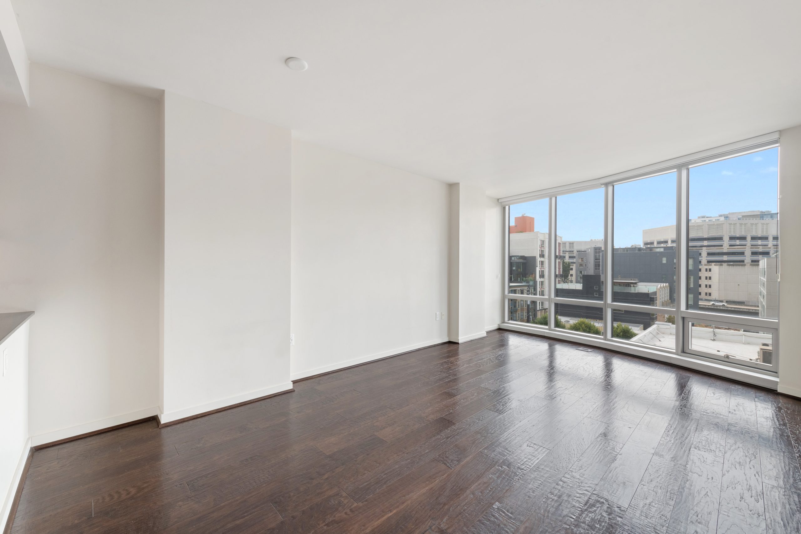 Living room with dark hardwood floors, floor-to-ceiling windows, and city views.