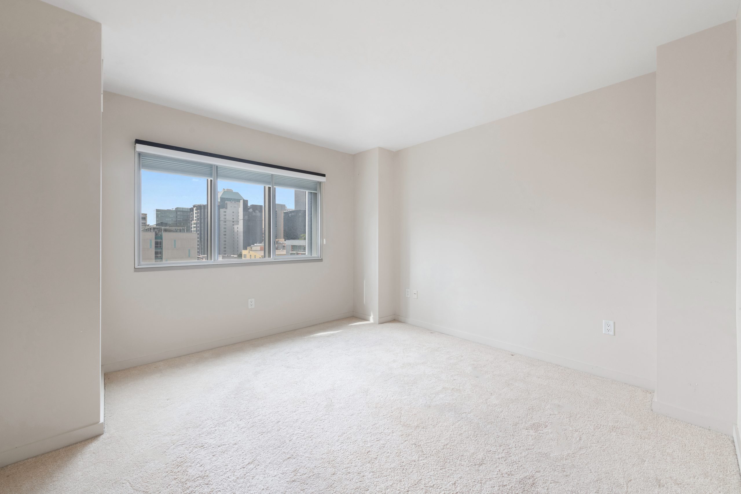 Bedroom with carpeted flooring, large window, and city skyline views.